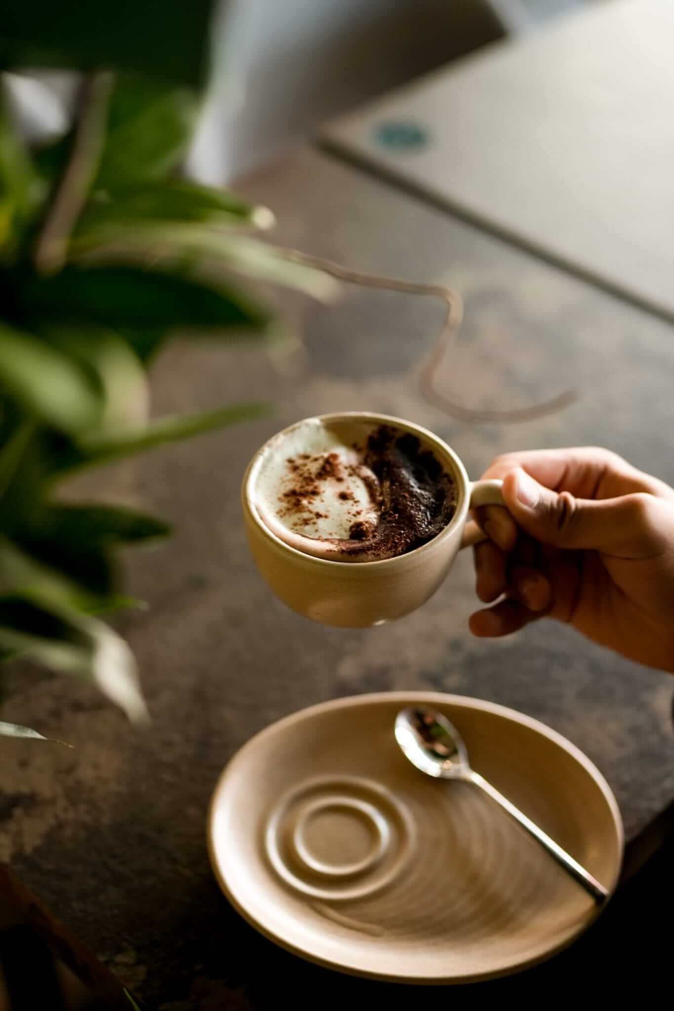 Hand holding Tove hot chocolate with cream swirl in beige ceramic cup