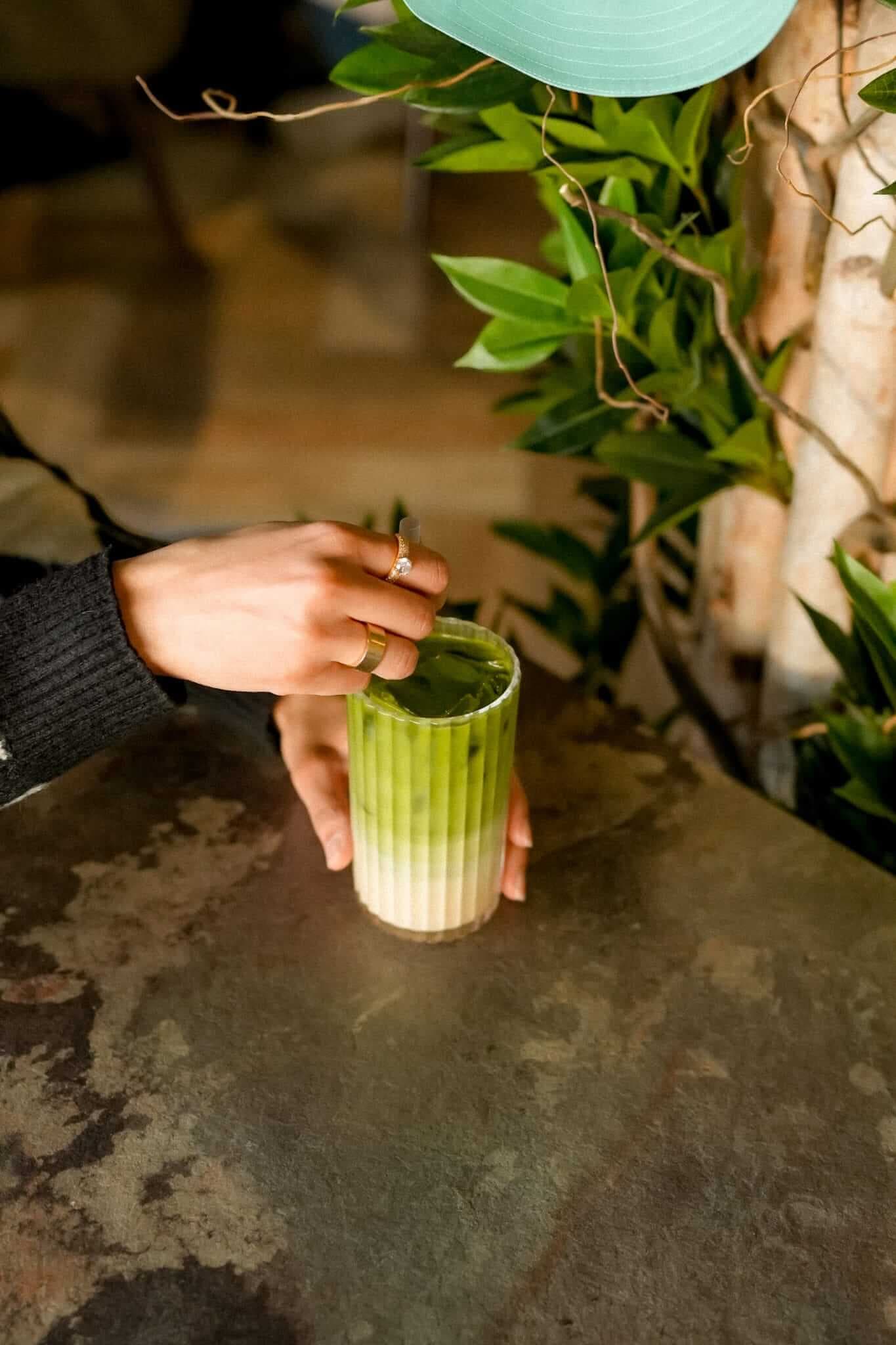 Hand stirring iced matcha latte in ribbed glass at TOVE café